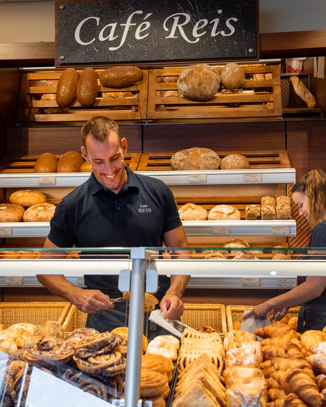 Freundlicher Mitarbeiter und Kollegin bedienen Kundschaft an der Backwaren-Theke im Café Reis Gewerbe-Süd Gilching