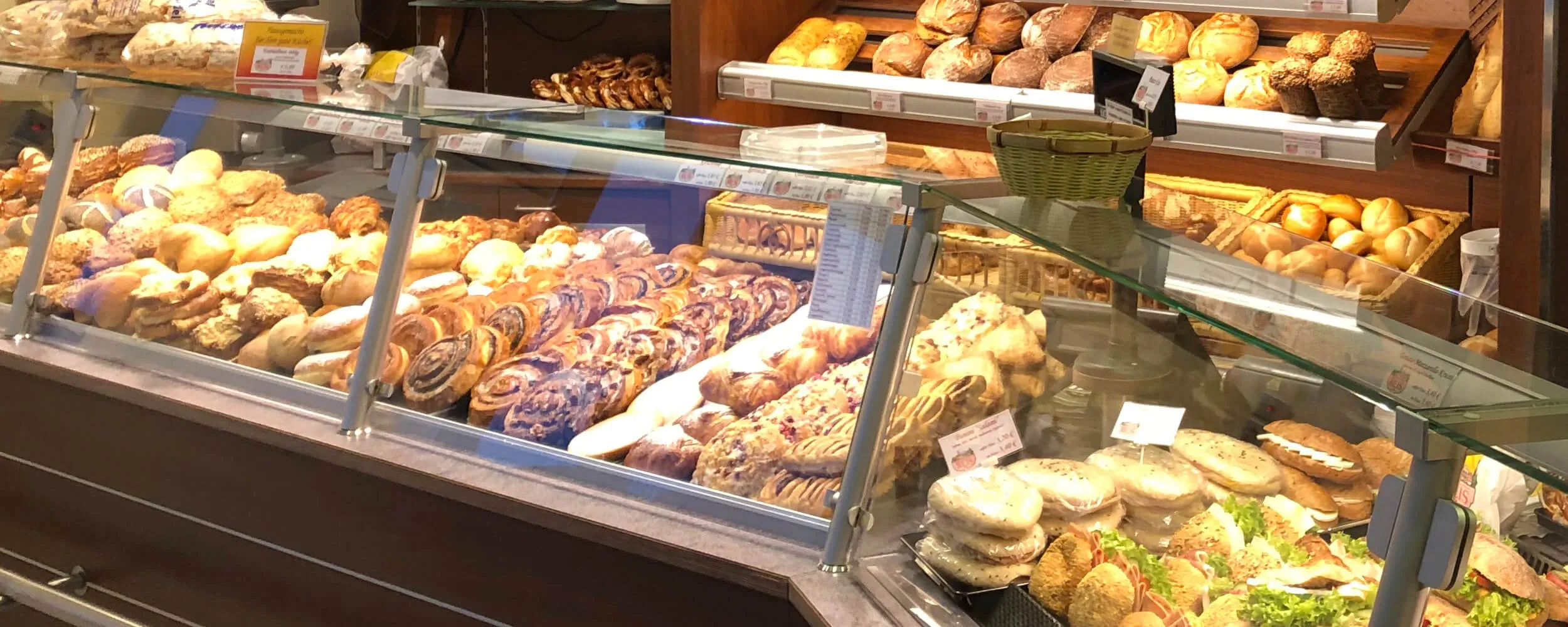 Große Bäckerei- und Konditoreiauslage im Café Reis Gewerbe-Süd Gilching mit Brötchen, Laugengebäck, Sandwiches und Brotregal