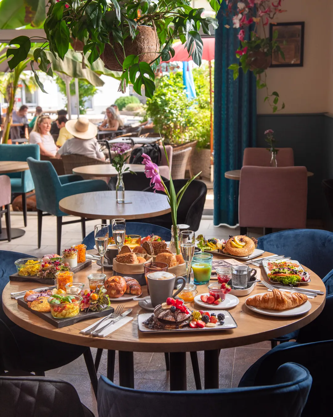 Reich gedeckter Brunch-Tisch im Café Reis Gilching mit Frühstücksbrett, Pancakes, Bagel, Salat, Kaffee und Blick zur Terrasse