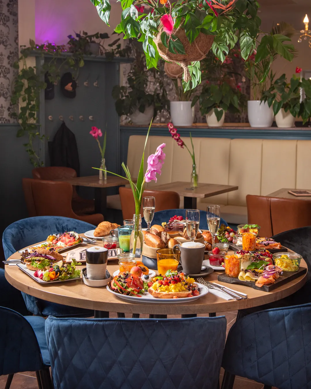 Opulenter Brunch-Tisch im Café Reis Gilching mit Frühstücksbrettern, Pancakes, Prosecco und Pink-Gladiole, blaue Samtstühle