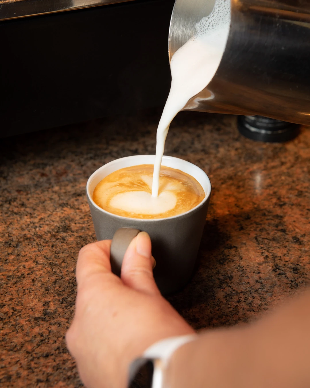 Frischer Cappuccino wird im Café Reis Gilching zubereitet – Milch wird in die Tasse gegossen