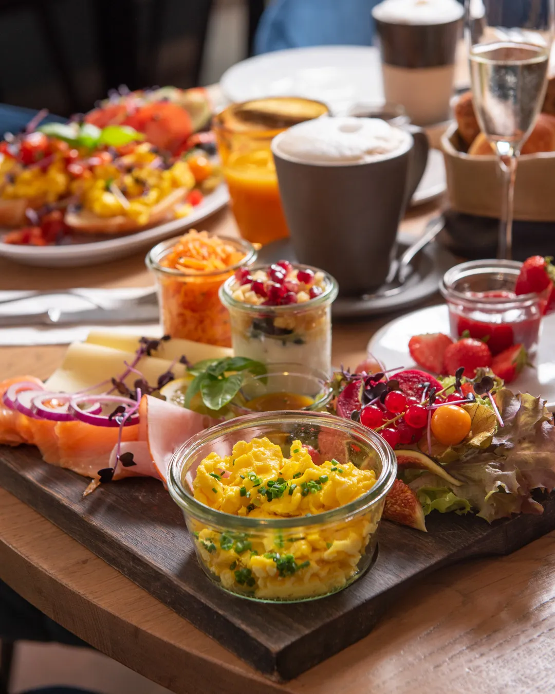Frühstücksbrett mit Rührei, Räucherlachs, Wurst, Käse, Joghurt und Karottensalat, dazu Cappuccino und Prosecco