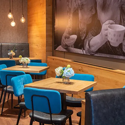 Gemütlicher Gastraum im Café Reis Gewerbe-Süd Gilching mit blauen Polsterstühlen, Holztischen und großformatigem Schwarz-Weiß-Foto