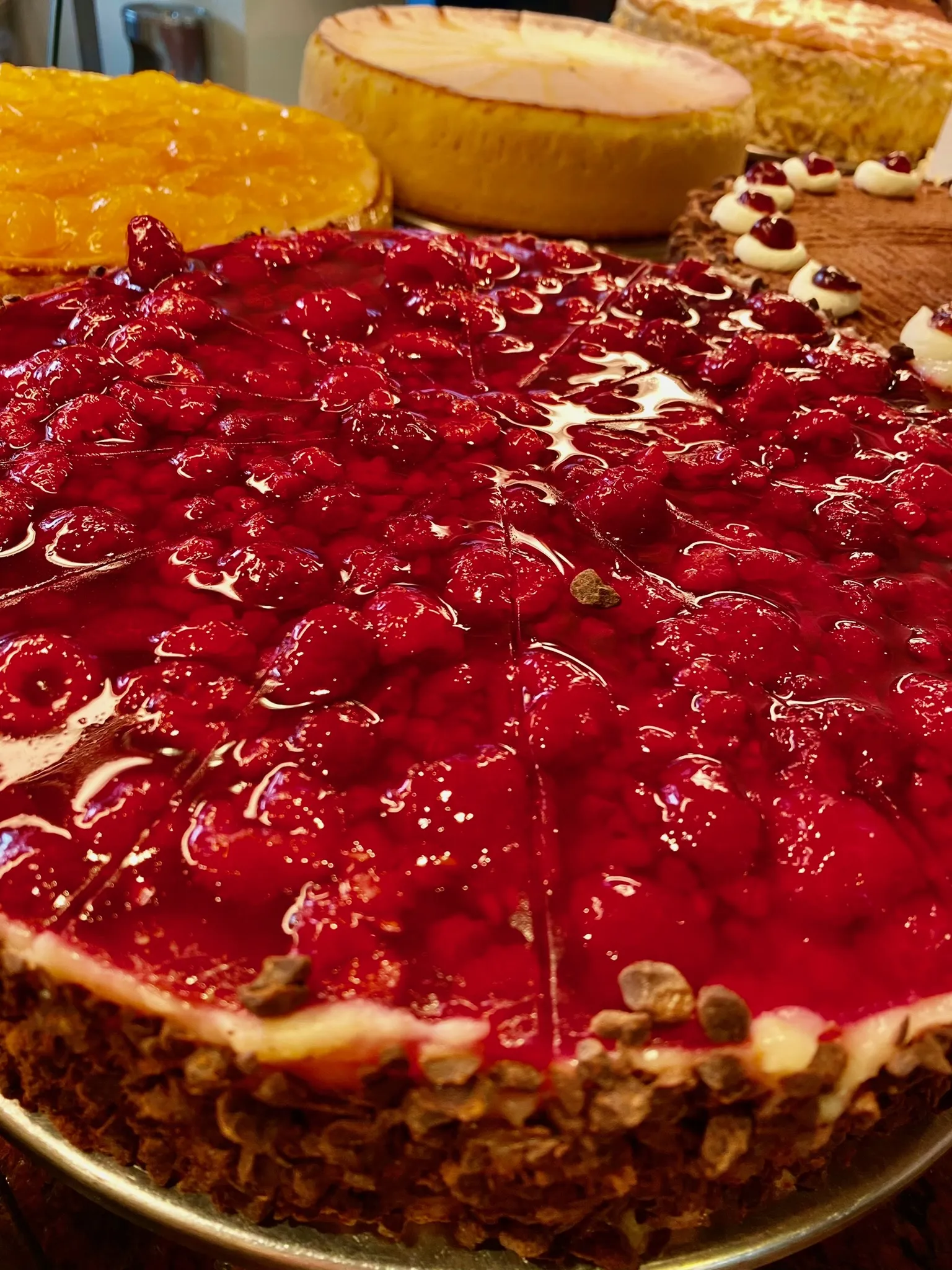 Glänzende Himbeertorte in der Kuchentheke im Café Reis Gilching, im Hintergrund Sanddorntorte, Käsekuchen und Schokoladentorte