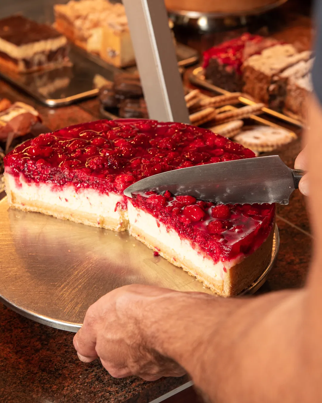 Johannisbeertorte wird in der Auslage des Café Reis Gilching frisch angeschnitten, weitere Kuchen und Torten im Hintergrund