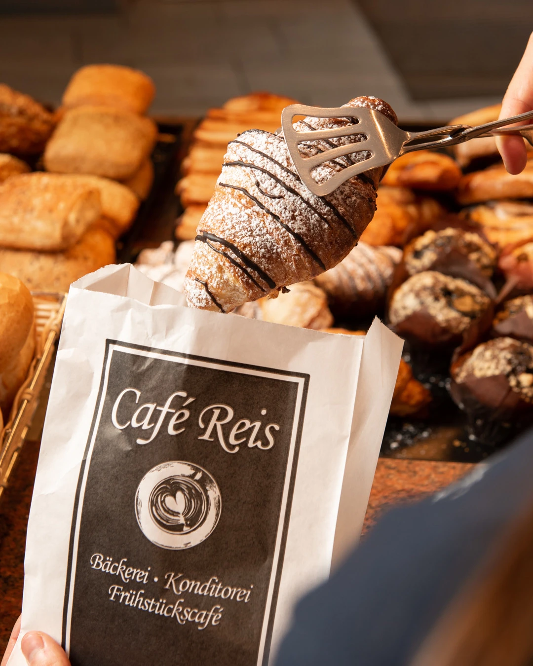 Frisches Schokocroissant wird in eine Café-Reis-Papiertüte verpackt – Bäckerei Gilching