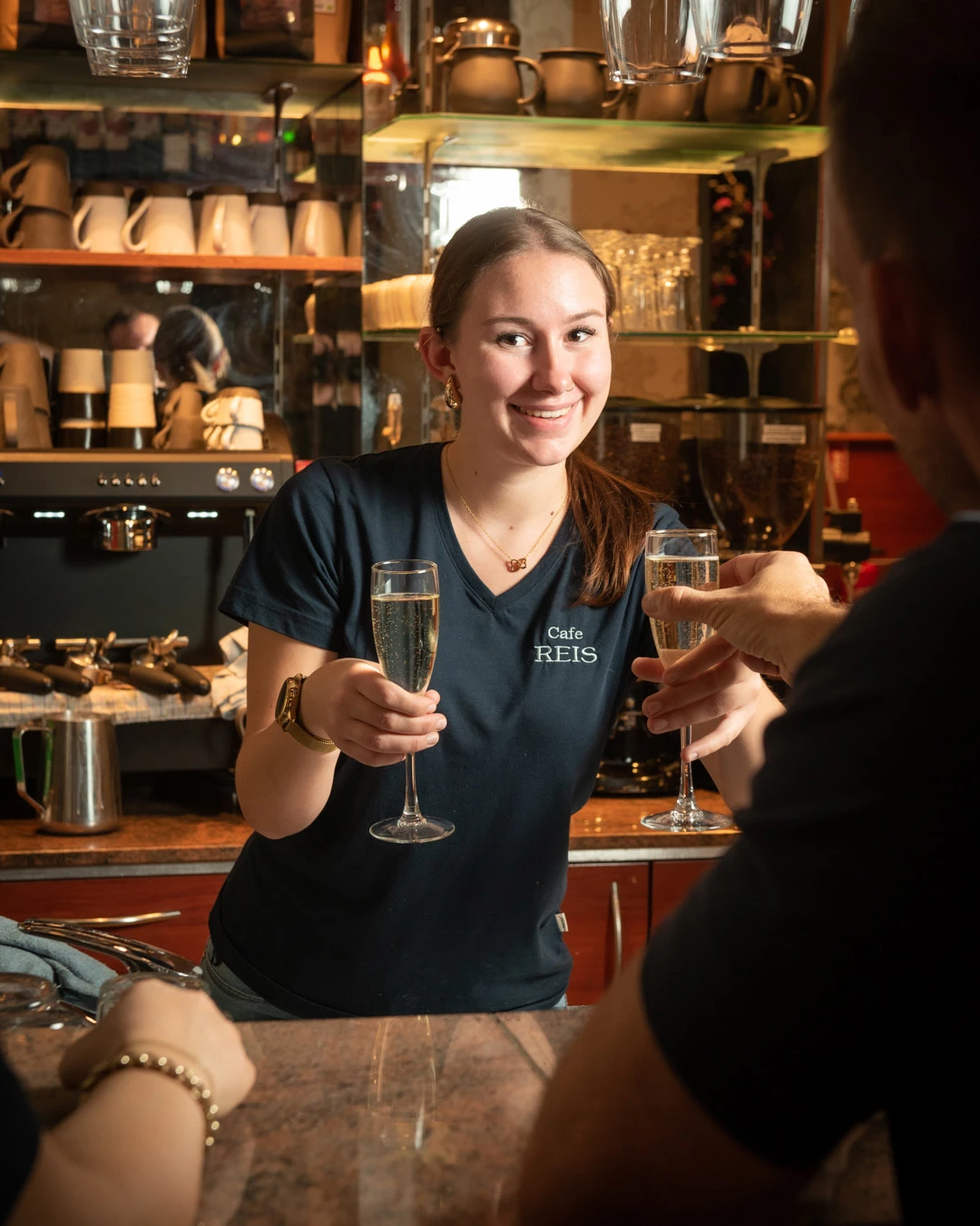 Mitarbeiterin im Café Reis Gilching stößt mit einem Gast mit Sekt an